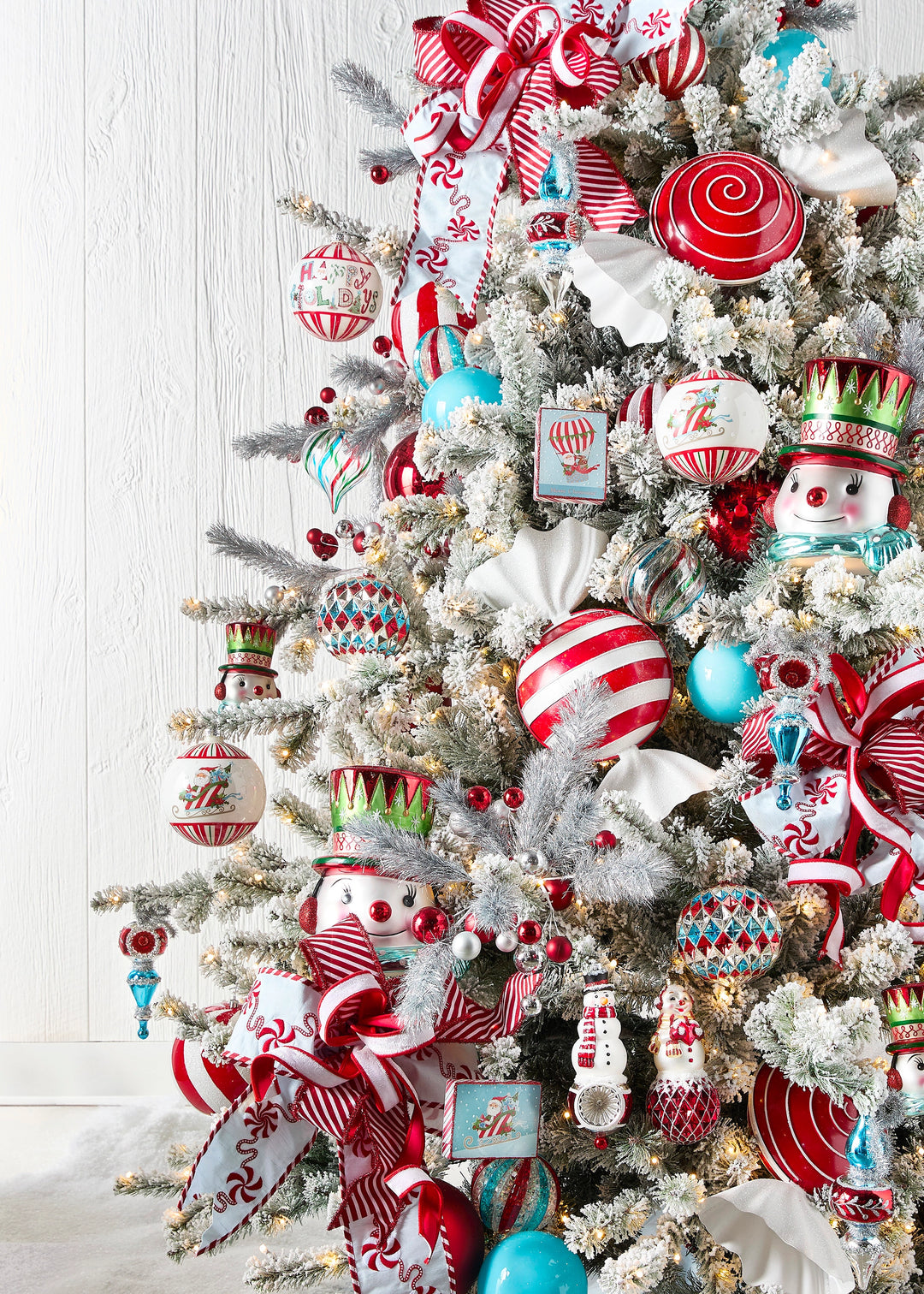 Frosted Christmas tree decorated with red, white, and turquoise Christmas ornaments, peppermint candy ribbon, striped wired ribbon, snowmen ornaments, and festive holiday décor.