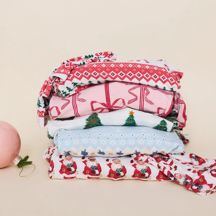 Christmas Tree Farm baby bamboo romper folded with festive holiday pajamas in a stack of Christmas prints.