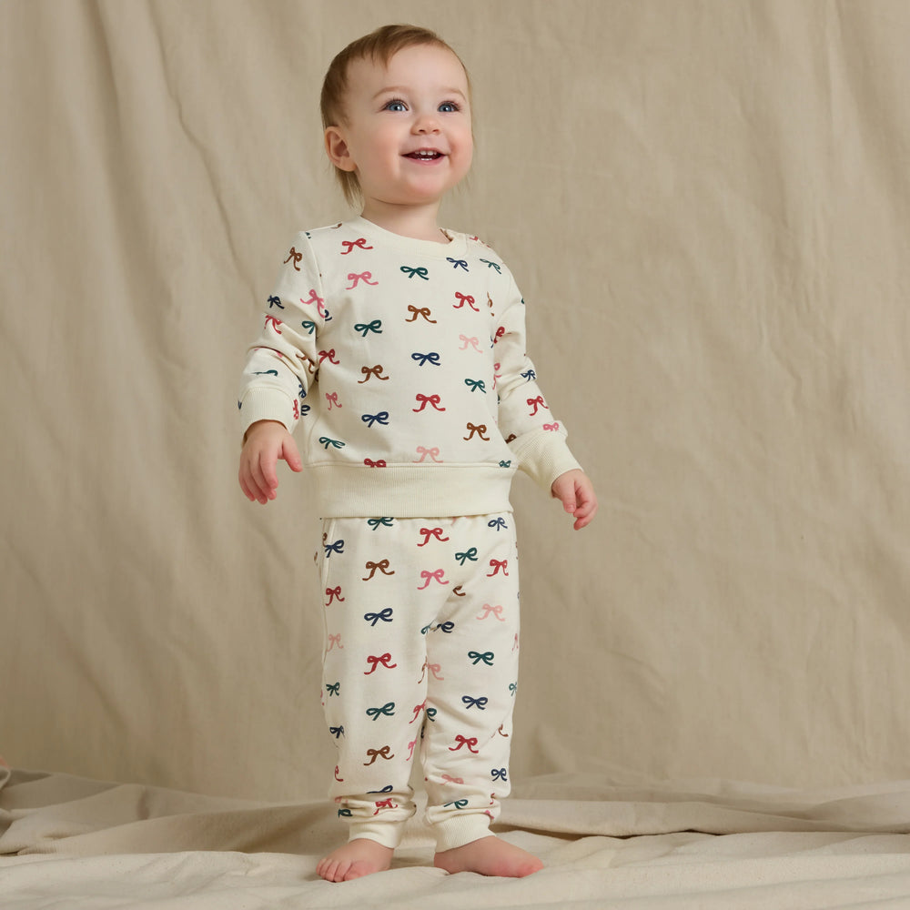 Baby wearing the cream Baby Bow Jogger Set with a multicolor bow print sweatshirt and matching jogger pants