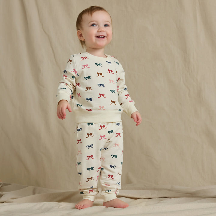 Baby wearing the cream Baby Bow Jogger Set with a multicolor bow print sweatshirt and matching jogger pants