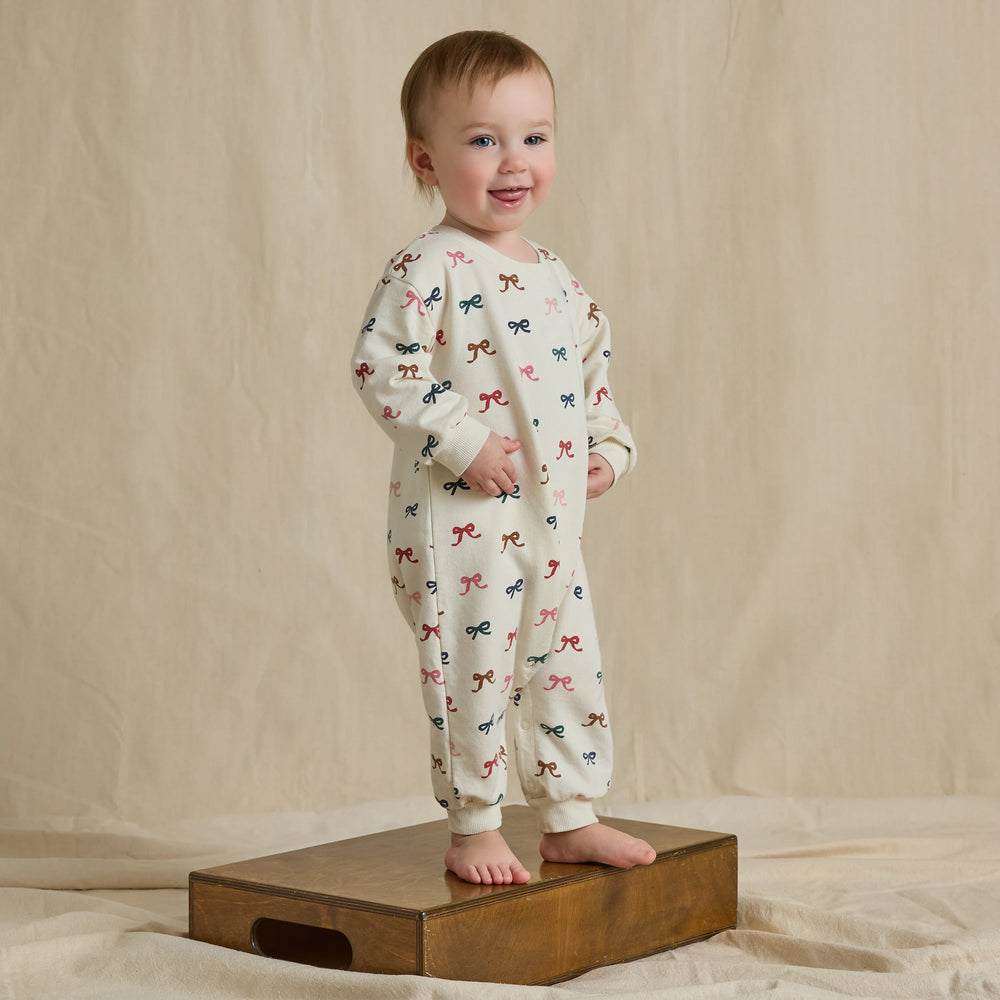 Baby wearing the cream Baby Bow Romper with colorful all-over bow print and long sleeves