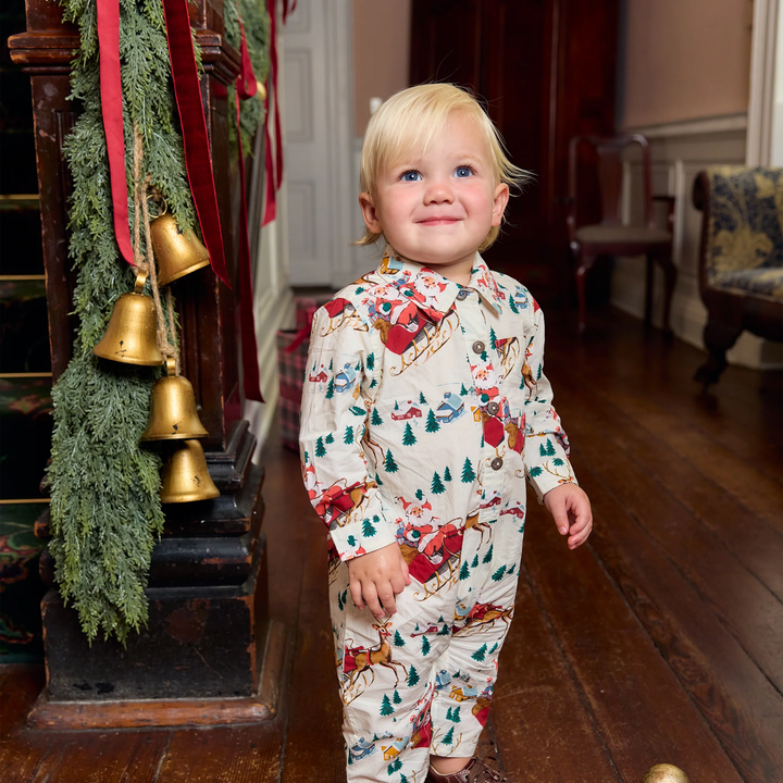 Toddler wearing Pink Chicken Santa Sleigh Easton Jumper beside Christmas garland and gold bells