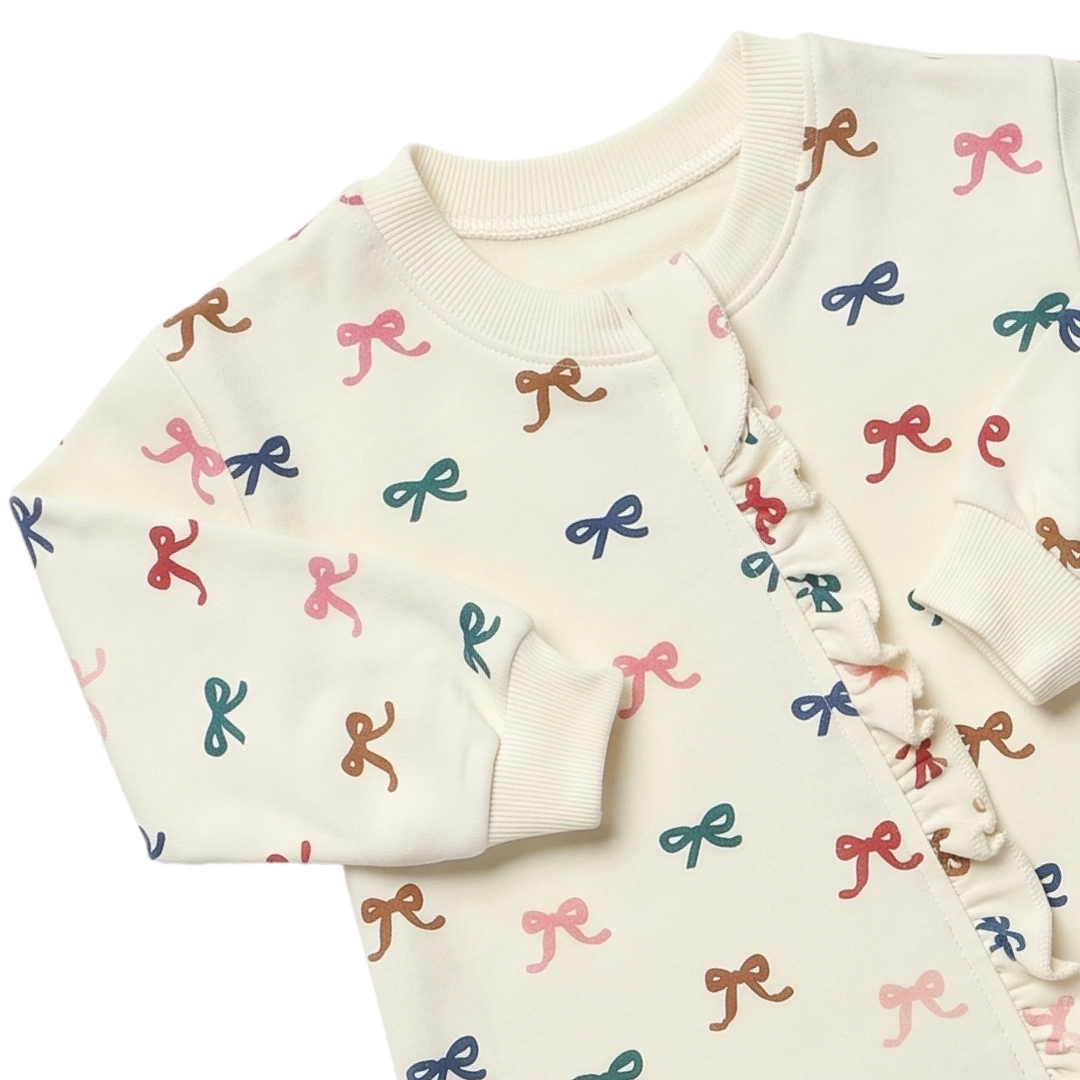Close-up of cream baby girl bow romper showing colorful bow print, ribbed neckline, sleeve cuffs and ruffle front detail