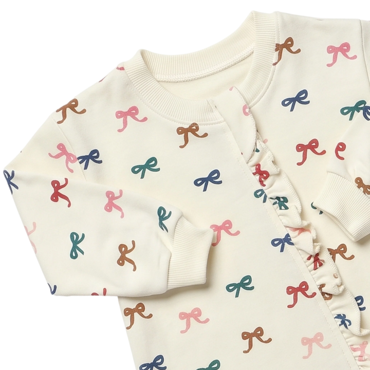 Close-up of cream baby girl bow romper showing colorful bow print, ribbed neckline, sleeve cuffs and ruffle front detail