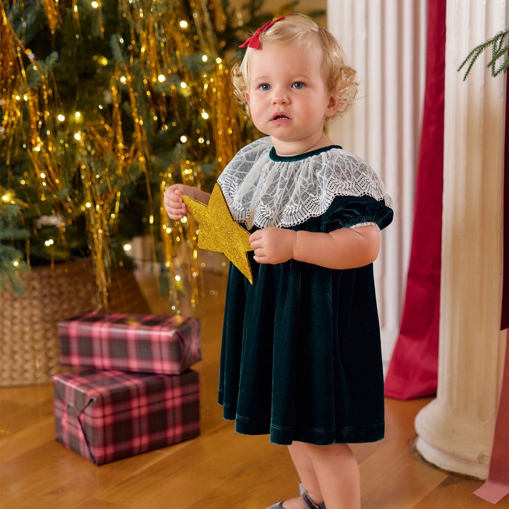 Baby girl wearing the Pink Chicken Caroline Dress in Evergreen Velour beside a decorated Christmas tree