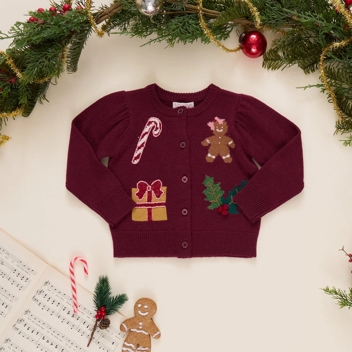 Pink Chicken Baby Girls Constance Sweater in burgundy displayed with festive Christmas greenery, ornaments, candy cane, and gingerbread cookie.