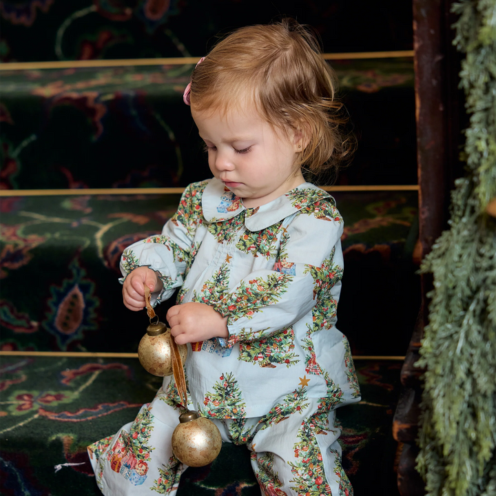 Baby girl wearing the Pink Chicken Dawson 2PC Set in Trees and Presents while sitting on a staircase and playing with gold Christmas ornaments.
