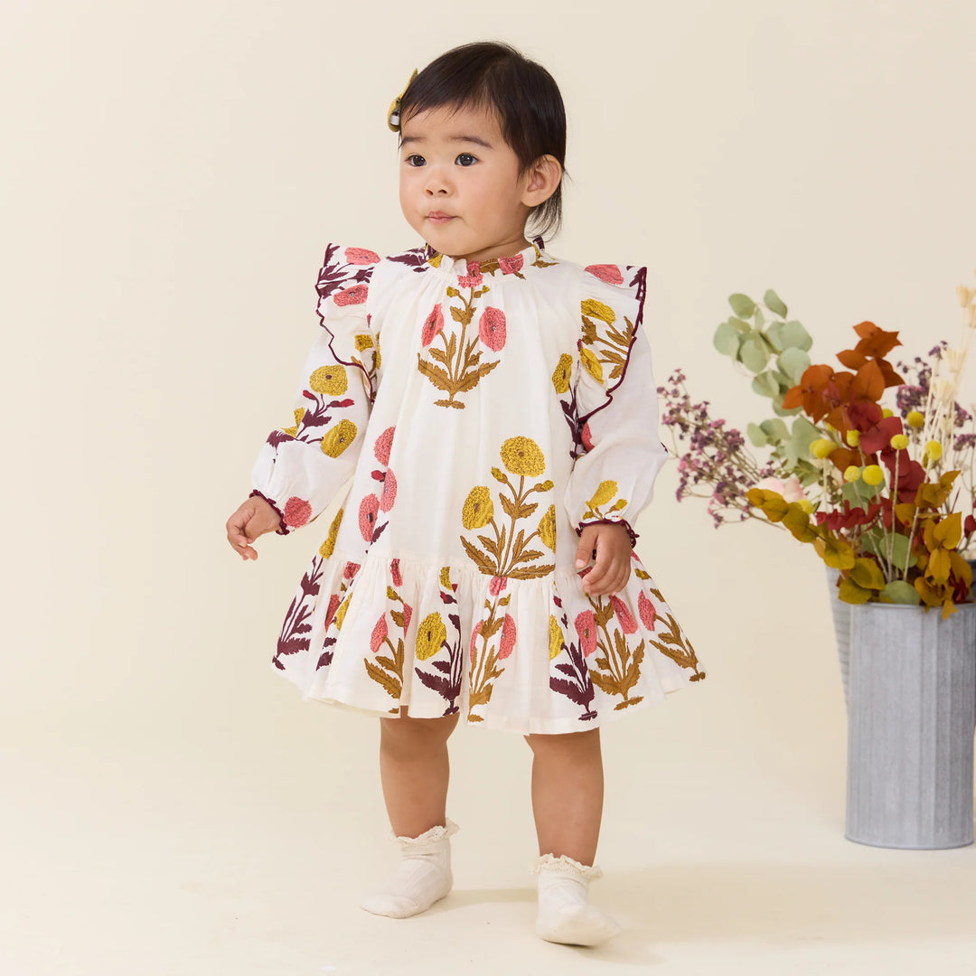 Baby girl wearing the Baby Girls Harvest Dandelion Dress with long sleeves and ruffle hem