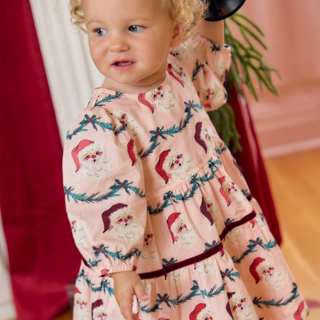 Baby girl modeling the Pink Chicken Maribelle Dress Set in Santa Garland with a pink Christmas print and burgundy velvet detailing.