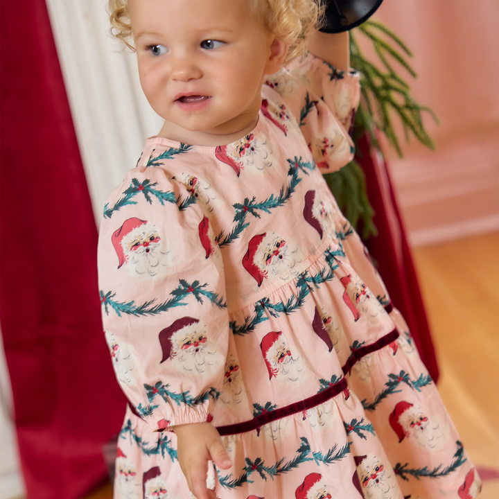 Baby girl modeling the Pink Chicken Maribelle Dress Set in Santa Garland with a pink Christmas print and burgundy velvet detailing.