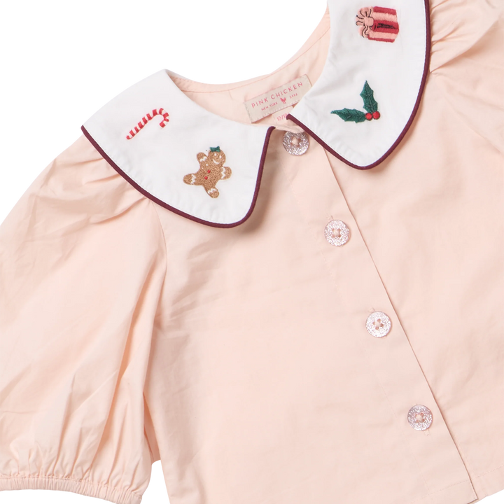 Close-up of the Baby Girls Noelle 2PC Set showing the white Peter Pan collar with embroidered candy cane, gingerbread man, holly, gift, and sparkling buttons.