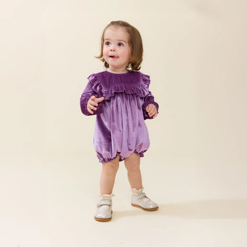 Baby girl wearing the Quinn Bubble Lavender Velour with ruffle bib and long sleeves