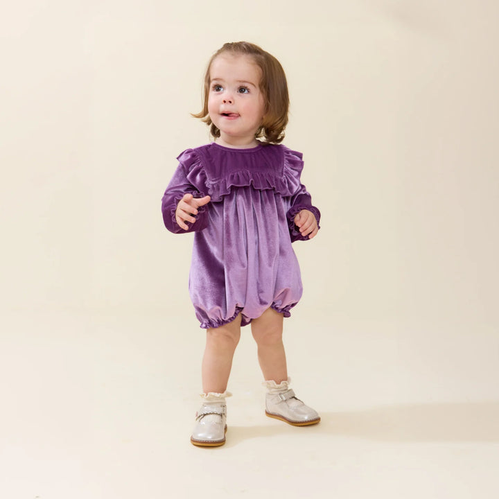 Baby girl wearing the Quinn Bubble Lavender Velour with ruffle bib and long sleeves