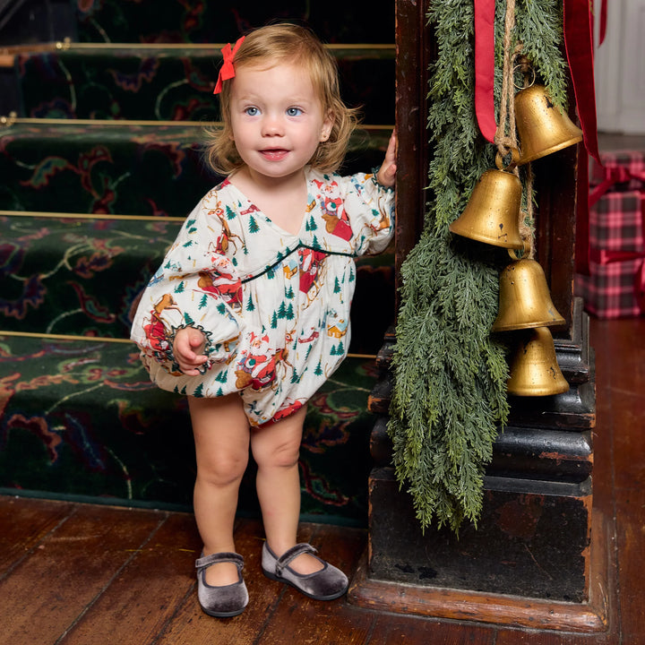 Toddler girl wearing Pink Chicken Wynne Bubble in Santa Sleigh beside festive Christmas garland and gold bells
