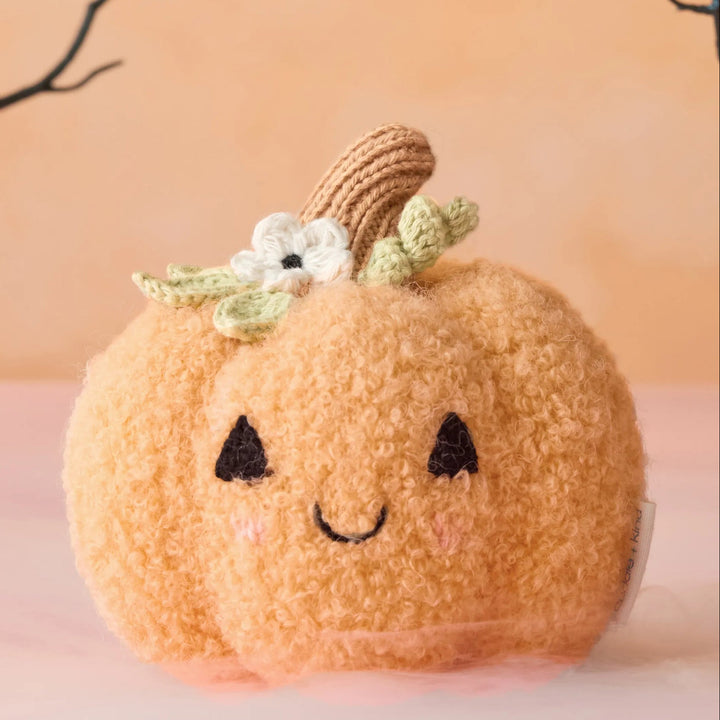 Baby Pumpkin Moonflower plush with curly orange texture, smiling face and knit floral details in a Halloween setting