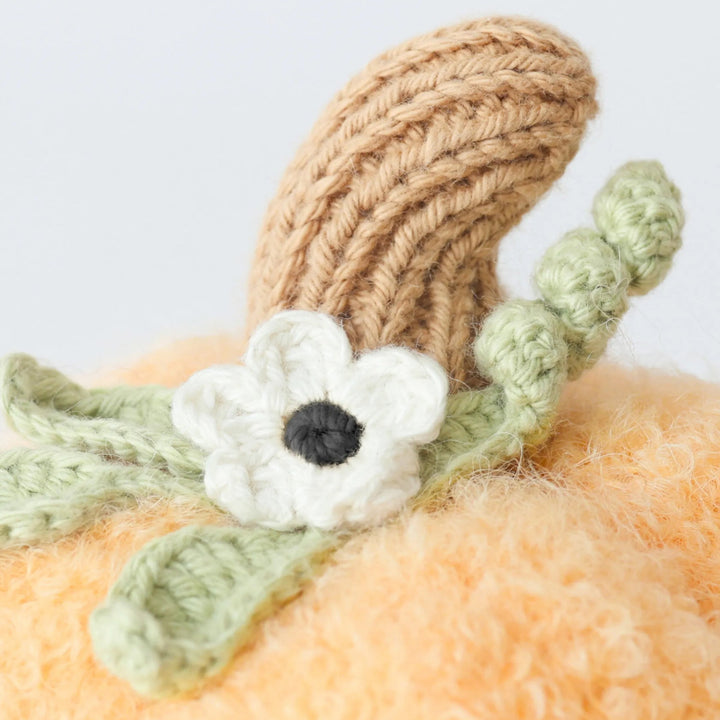 Close-up of Baby Pumpkin Moonflower plush featuring a knit brown stem, green leaves and white flower detail