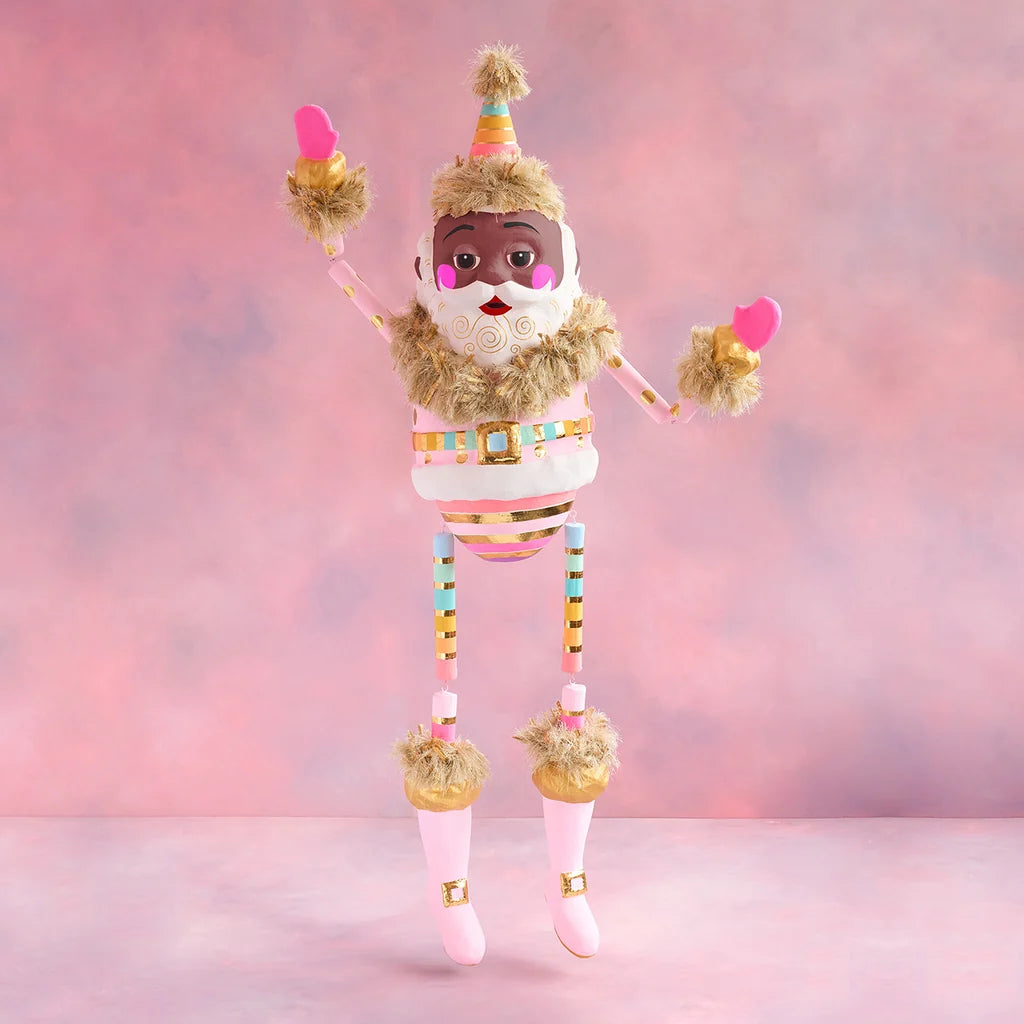 Rainbow Papa Noel Christmas display with black skin, a pastel striped suit, gold accents, pink boots, and raised arms against a soft pink holiday backdrop.