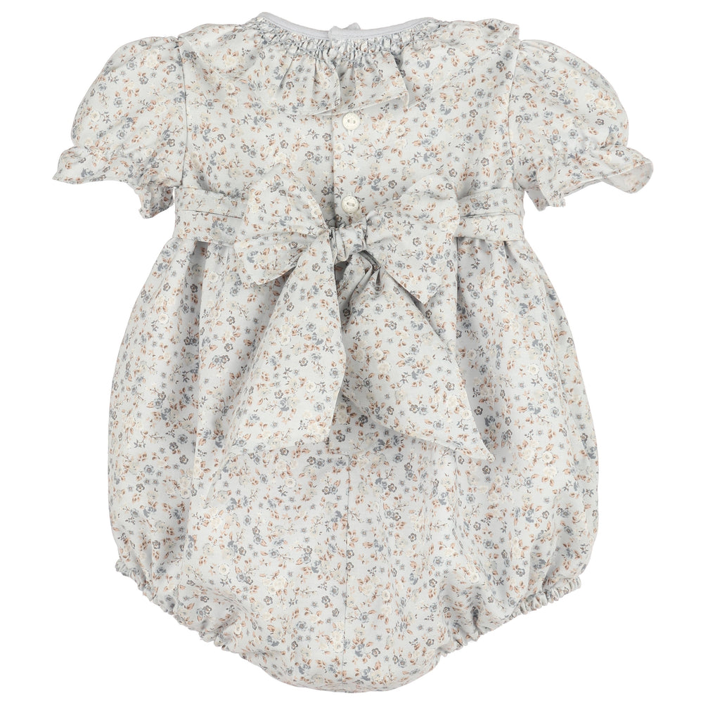 Back view of Bloomy Chintz Blue Smocked Bubble featuring a delicate floral print, ruffle collar, puff sleeves, button closure, and large tie-back bow.