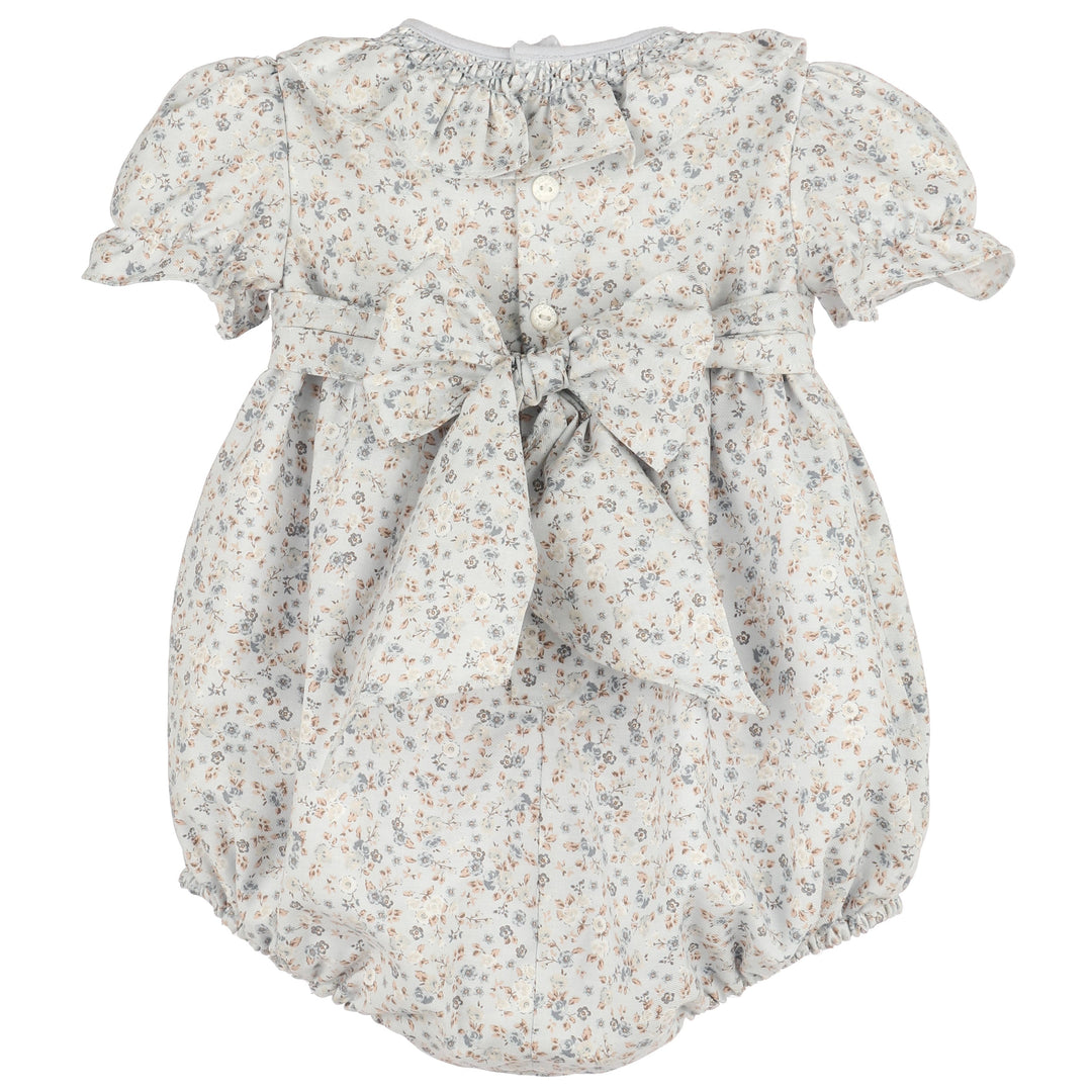 Back view of Bloomy Chintz Blue Smocked Bubble featuring a delicate floral print, ruffle collar, puff sleeves, button closure, and large tie-back bow.