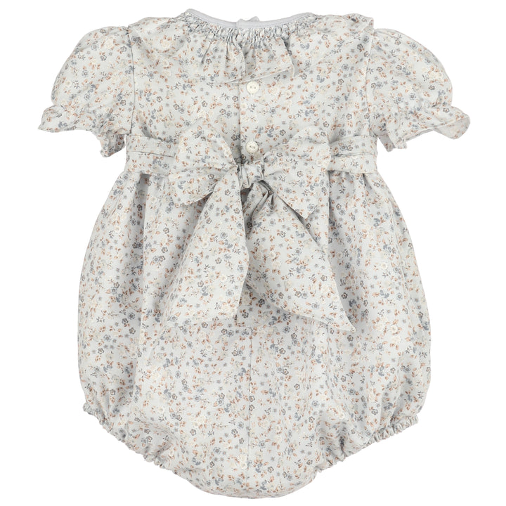 Back view of Bloomy Chintz Blue Smocked Bubble featuring a delicate floral print, ruffle collar, puff sleeves, button closure, and large tie-back bow.