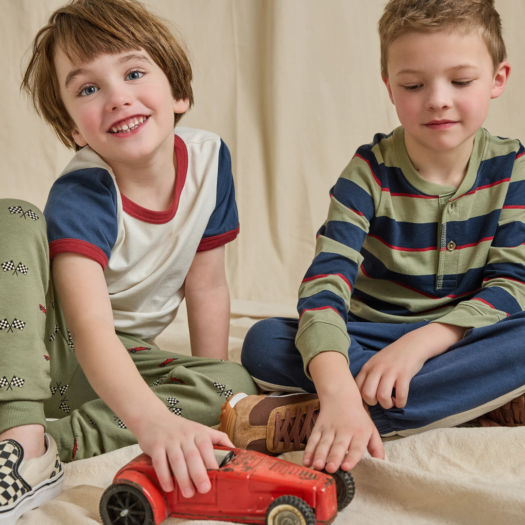Boy wearing an olive green and navy striped Henley shirt with blue pants in a casual kids lifestyle setting.