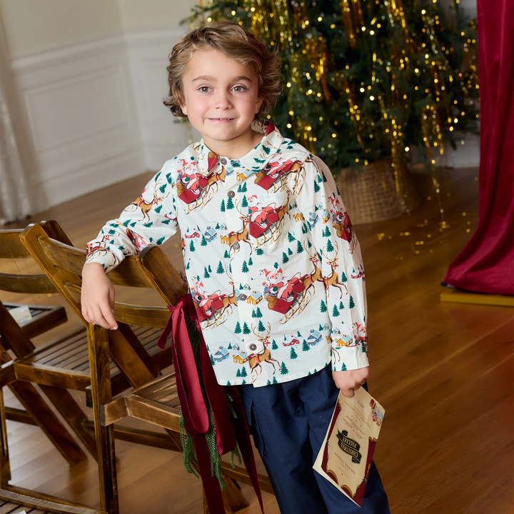 Boy wearing Pink Chicken Santa Sleigh Jack Shirt beside a decorated Christmas tree