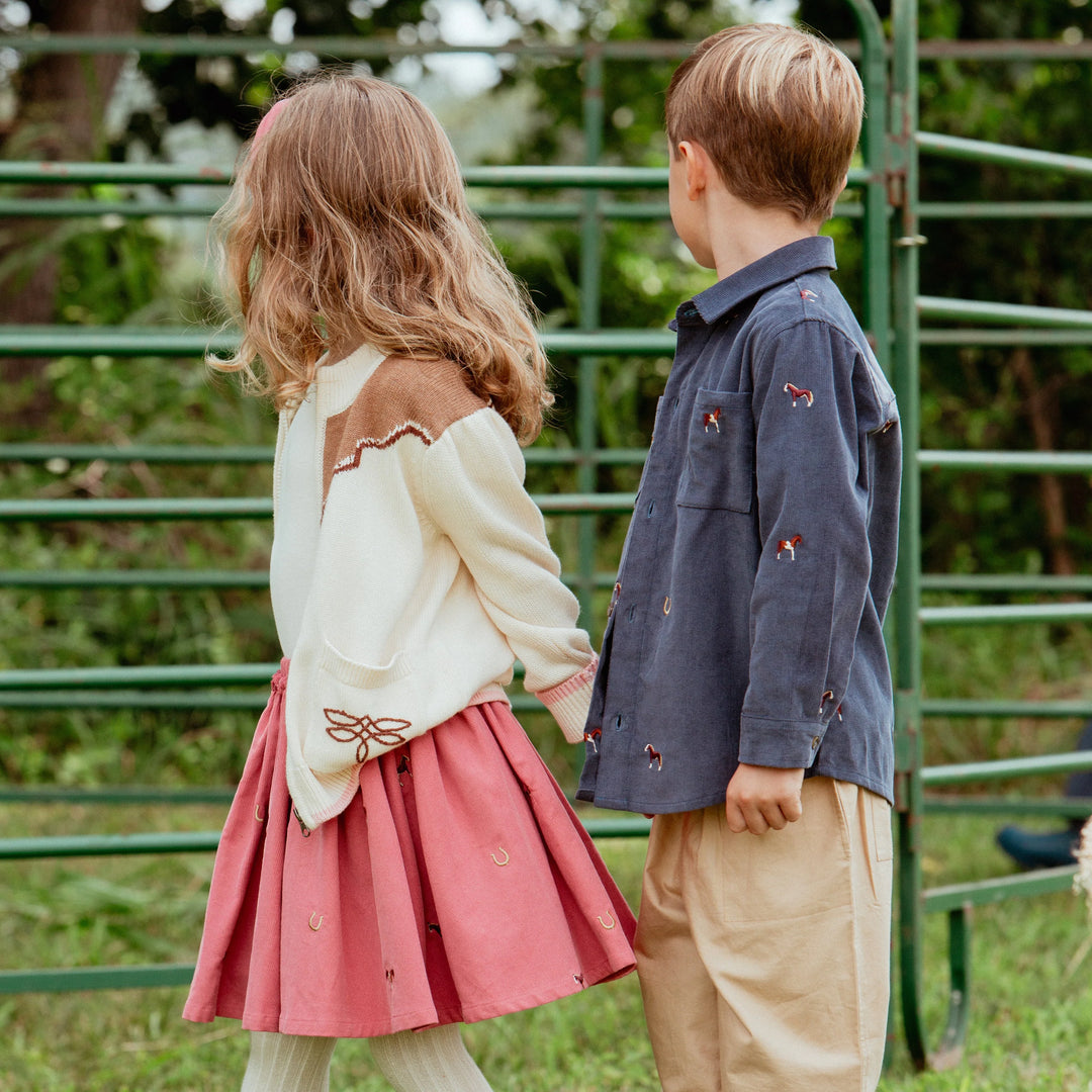 Boy wearing a navy horse embroidered button-down shirt with khaki pants outdoors
