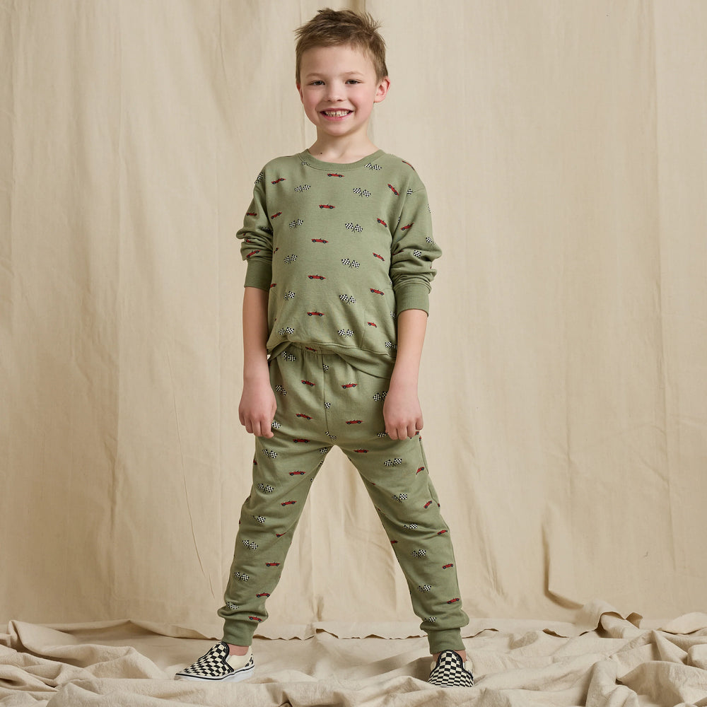 Boy wearing olive green race car jogger pants with matching sweatshirt and checkered slip-on shoes