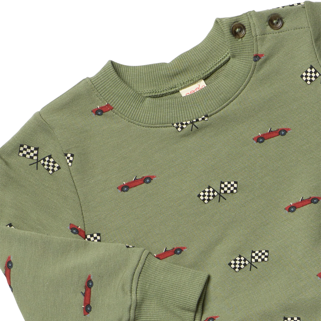 Close-up of olive green boys sweatshirt featuring red race cars, black and white checkered flags, ribbed trim and shoulder buttons.