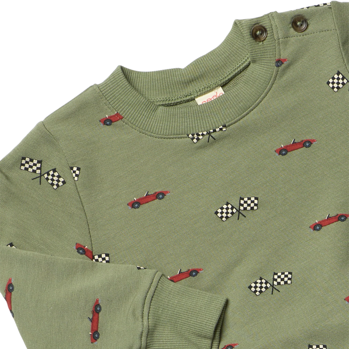 Close-up of olive green boys sweatshirt featuring red race cars, black and white checkered flags, ribbed trim and shoulder buttons.
