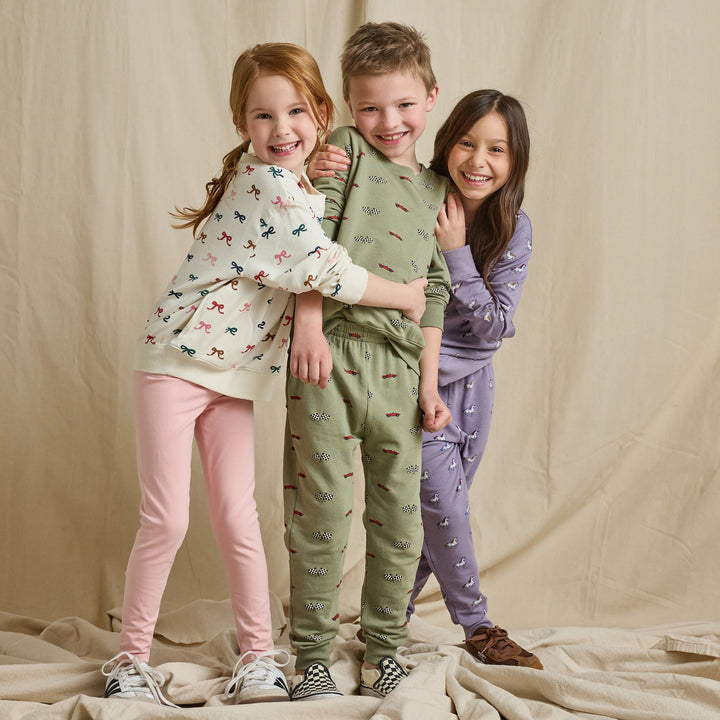 Boy wearing an olive green race car and checkered flag sweatshirt with matching pants in a kids clothing lifestyle image.