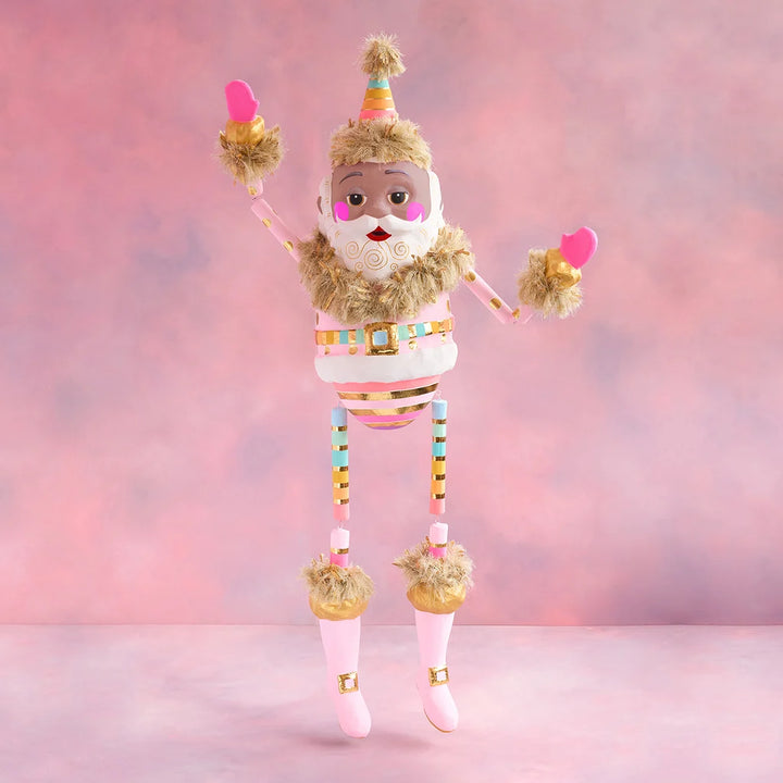Rainbow Papa Noel Christmas display with brown skin, a pastel striped suit, gold accents, pink boots, and raised arms against a soft pink holiday backdrop.