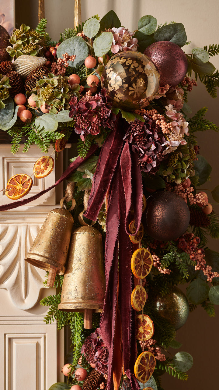 Burgundy velvet torn edge ribbon styled on an elegant Christmas garland with gold bells, ornaments, eucalyptus, pinecones, berries, hydrangeas, and dried oranges.
