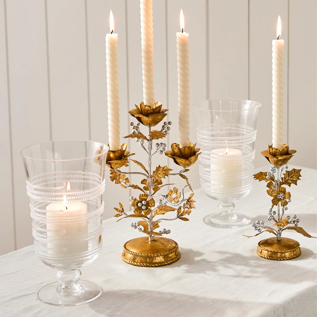Clear glass hurricane candle holders styled with pillar candles alongside gold floral candlesticks