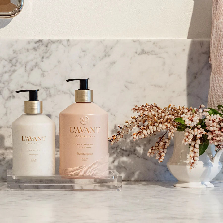 Clear lucite bathroom tray styled with hand soap and hand lotion beside fresh flowers for a clean, elegant vanity display.