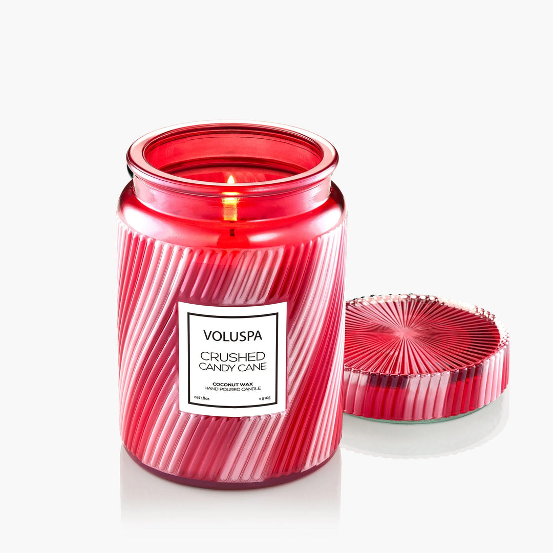 Lit Voluspa Crushed Candy Cane Large Jar Candle with decorative red glass lid displayed beside the jar