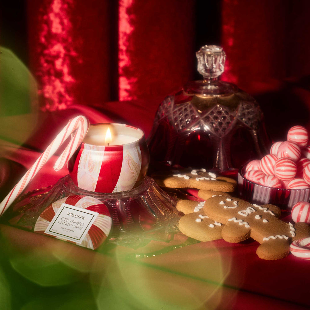 Crushed Candy Cane Mini Tin Candle lit among candy canes, peppermint candies and festive Christmas décor