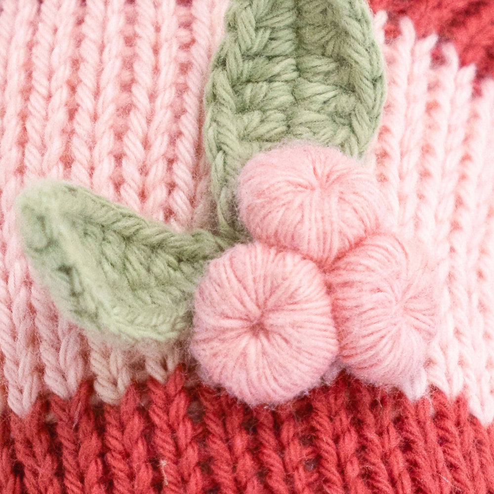 Close up image of the detailing on Cuddle+Kind's Christmas Baby Candy Cane in the color scheme, blush stripe. Featuring its three berry and leaf "bow" detailing. 