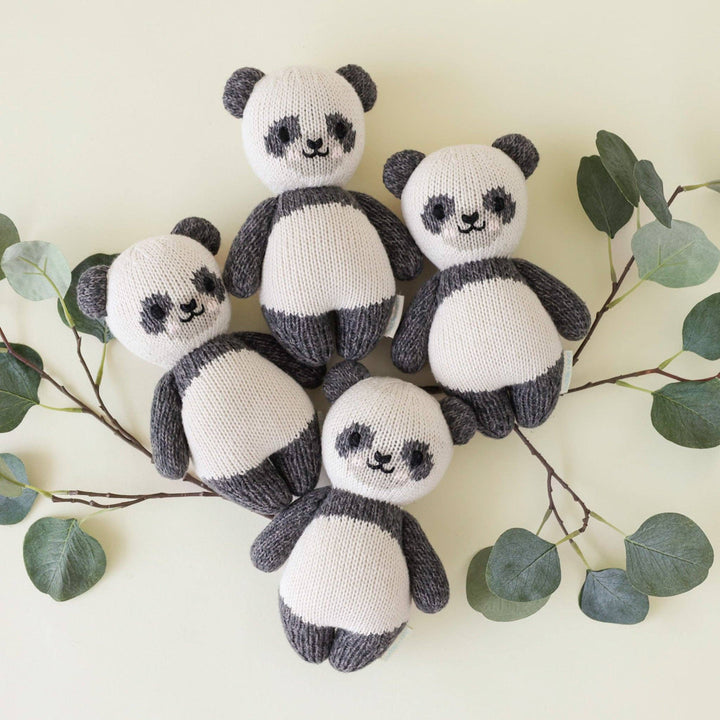 Four Cuddle+Kind Baby Panda plush staged with sage branches