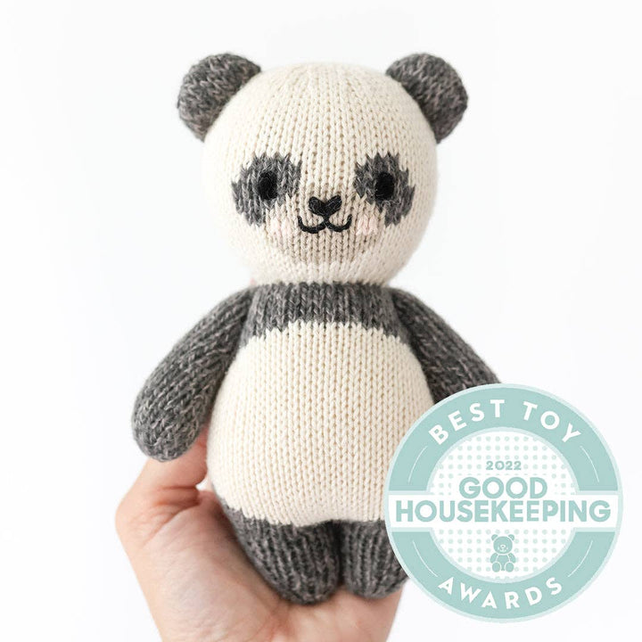 Cuddle+Kind Baby Panda plush held by a hand, with a Best Toy housekeeping award in the lower right