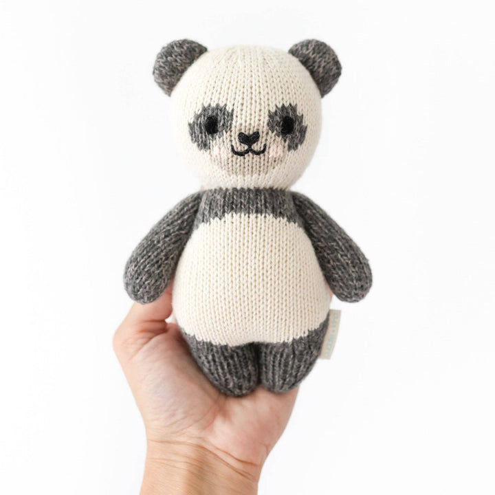Cuddle+Kind Baby Panda plush held by a hand on a white background