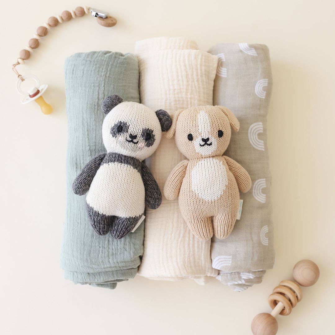Cuddle+Kind Baby Panda plush staged with Baby Puppy on baby swaddles