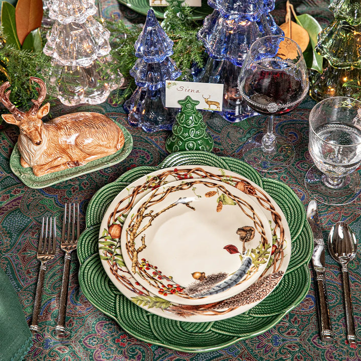 Deer Christmas place card displayed on an elegant woodland Christmas tablescape with green dinnerware and glass trees.