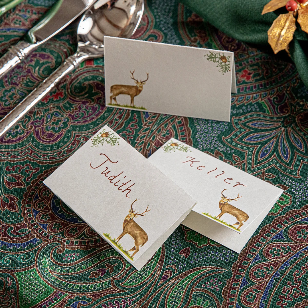 Deer Christmas place cards personalized with guest names and styled on a green paisley holiday table setting.