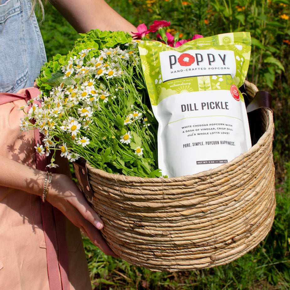 Poppy Dill Pickle Hand-Crafted Popcorn displayed in a basket with fresh flowers
