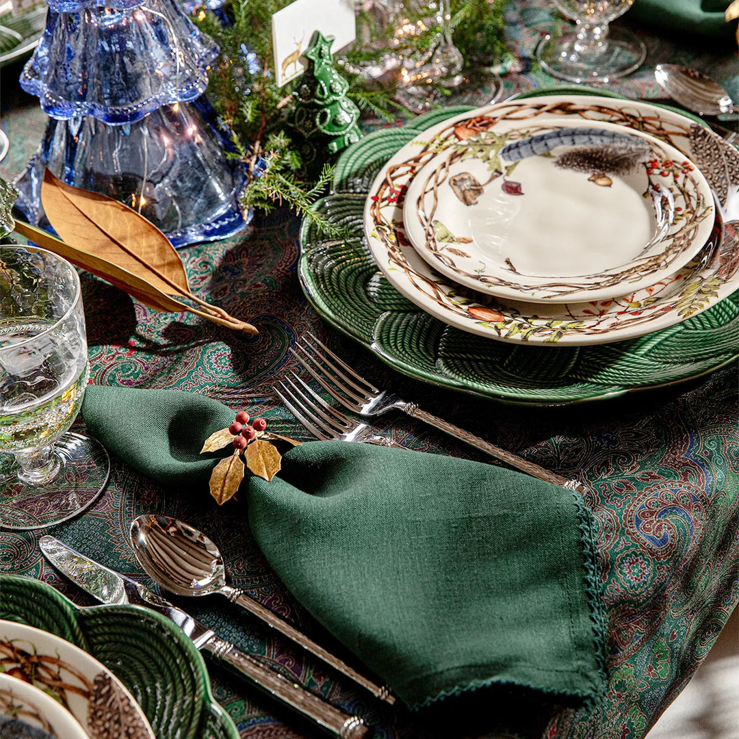 Forest green linen napkin styled on an elegant woodland Christmas table with green dinnerware and festive décor.