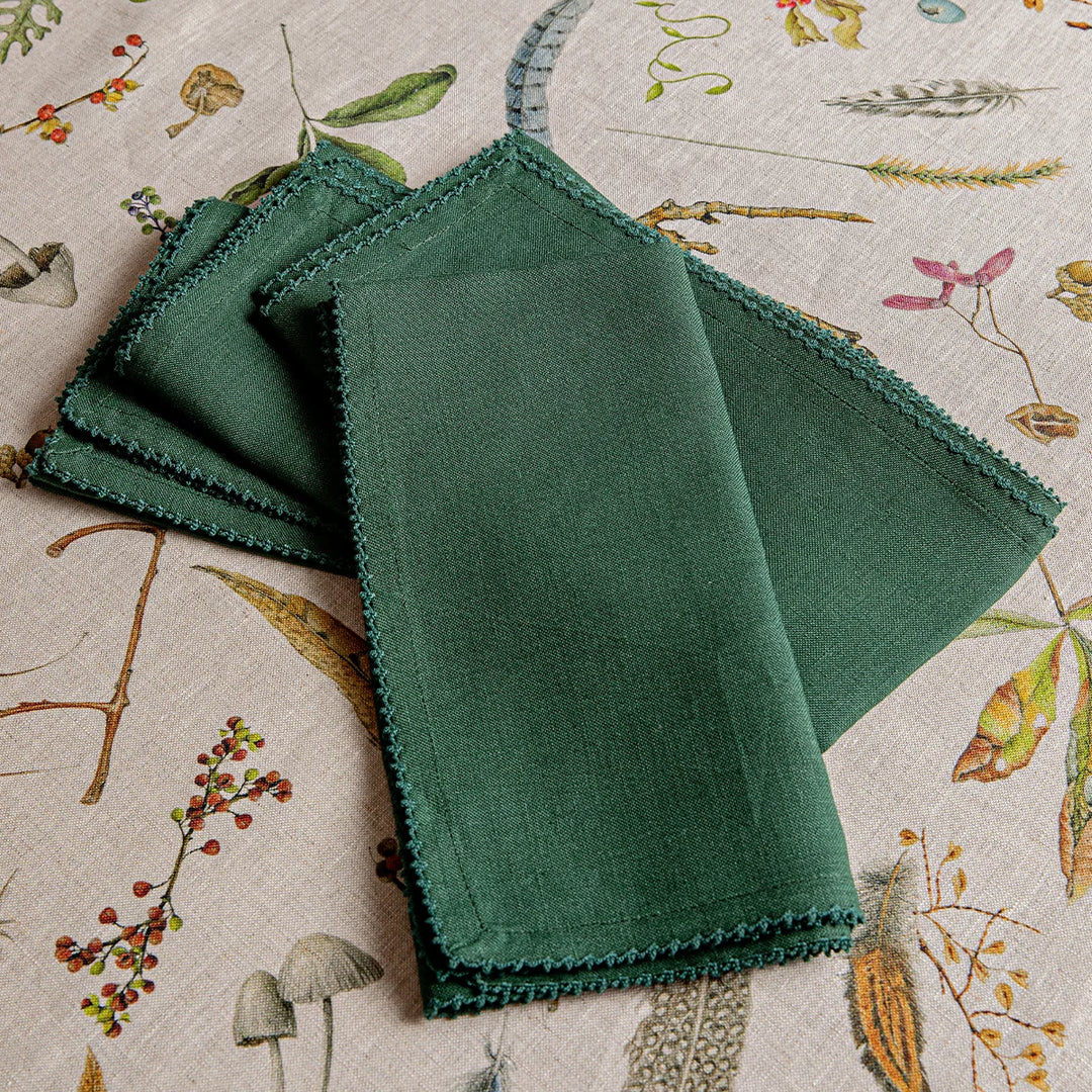 Close-up of folded forest green linen napkins showing the woven fabric texture and delicate decorative edge trim.