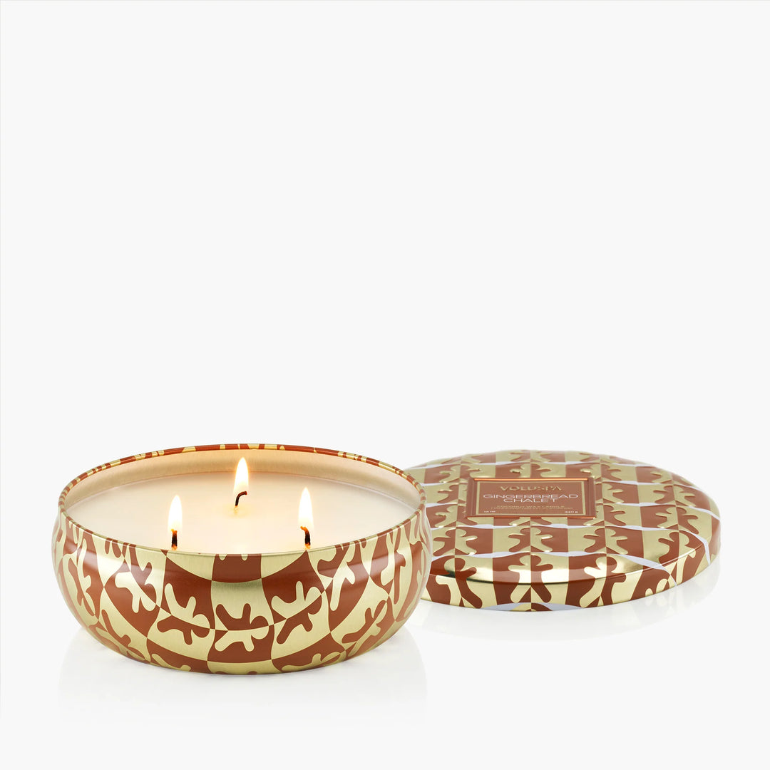 Lit Voluspa Gingerbread Chalet 3 Wick Tin Candle with three wicks and decorative brown and gold lid