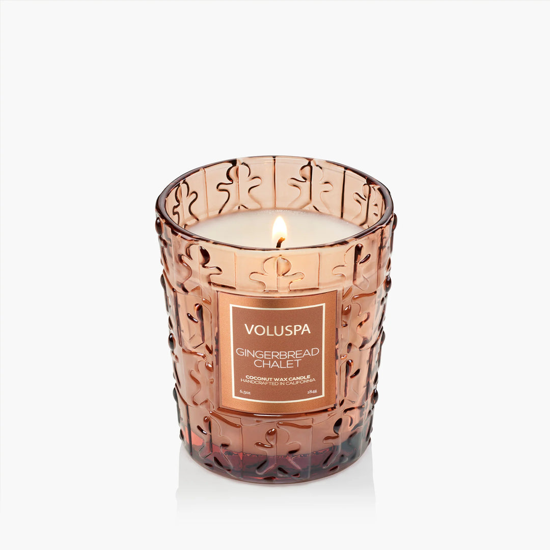 Lit Voluspa Gingerbread Chalet Classic Candle in embossed amber glass with gingerbread design