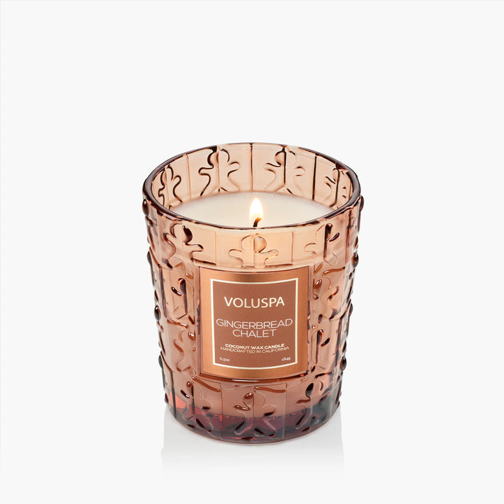 Lit Voluspa Gingerbread Chalet Classic Candle in embossed amber glass with gingerbread design